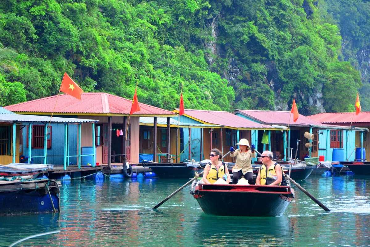 Floating Homes and Bamboo Boat Tour in Ba Hang Visitors explore Ba Hang Fishing Village by bamboo boat, passing floating houses with Vietnamese flags and colorful structures.