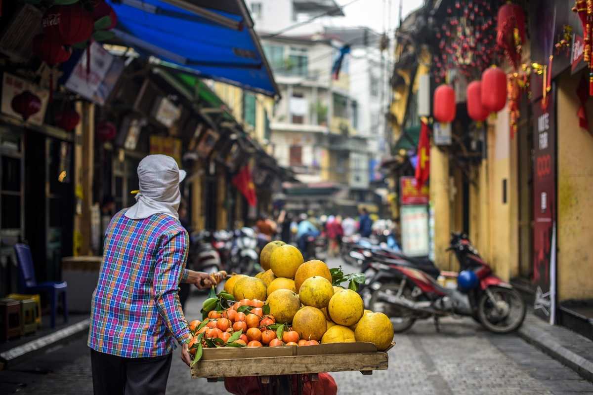 Local street vendor with fruit cart in Hanoi Old Quarter Local vendor pushing cart loaded with fresh fruits on a busy street in the Hanoi Old Quarter