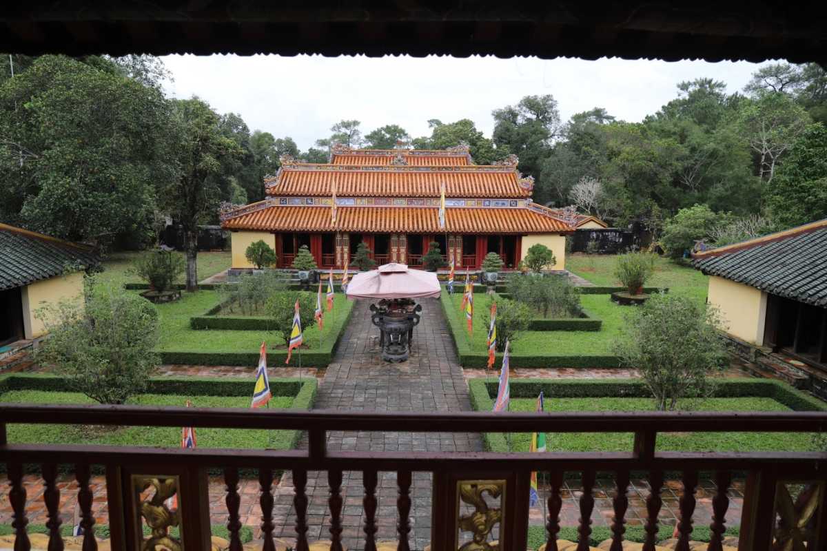 Courtyard and Main Hall from Balcony Perspective View of Gia Long Tomb's main hall and garden courtyard from balcony with flags, green lawns, and tiled roofs in Hue.