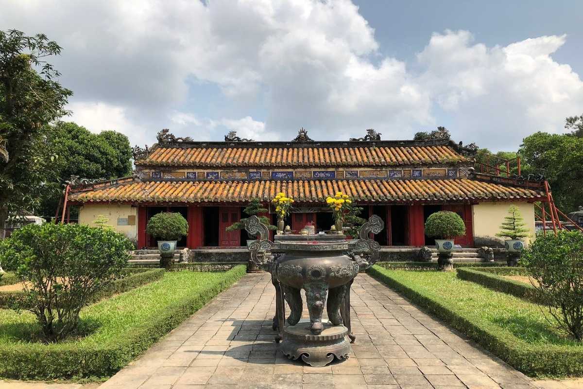 Gia Long Tomb Main Ancestral Hall and Courtyard Gia Long Tomb main ancestral hall with tiled roof, incense urn, yellow flowers, and gardens in Hue, Vietnam.