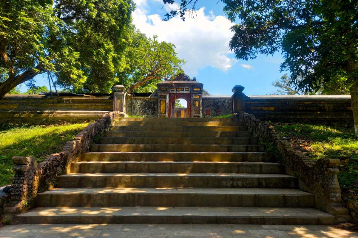 Ancient Stone Stairway and Ceremonial Gate Ancient stone stairway leading to a ceremonial gate shaded by trees at Gia Long Tomb in Hue, Vietnam.