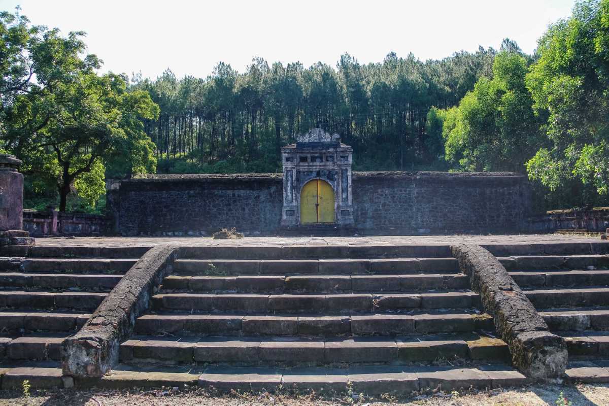 Stone Wall Gate and Forest at Gia Long Tomb Stone wall with yellow gate surrounded by pine forest and old stone steps at Gia Long Tomb in Hue, Vietnam.