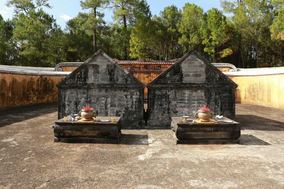 Twin Tombs of Gia Long and Empress Thua Thien Cao Twin stone tombs with incense urns at Gia Long Tomb, set within circular yellow walls and pine trees in Hue, Vietnam.