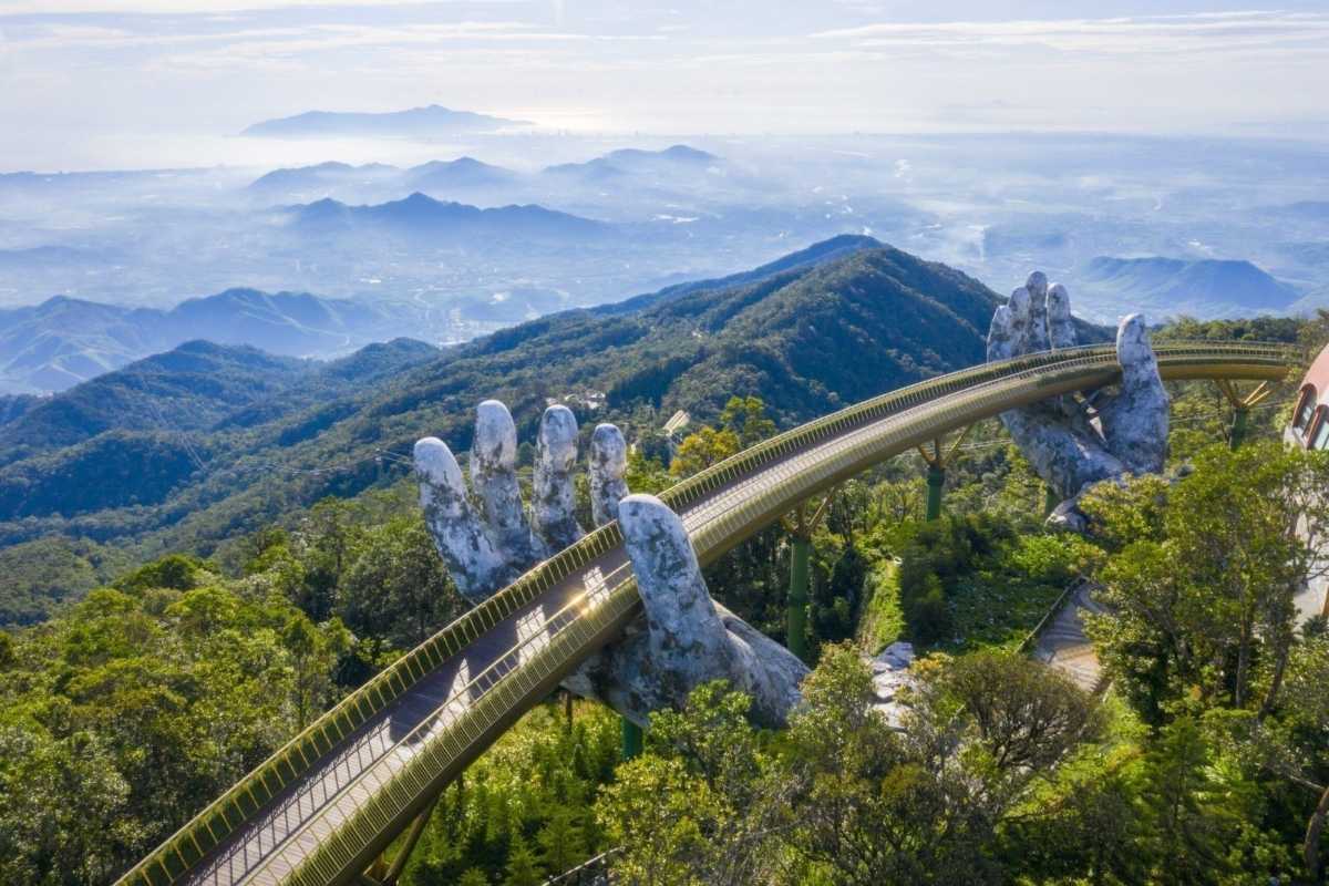 Golden Bridge Da Nang aerial view misty green hills Aerial view of Golden Bridge Da Nang stretching above misty green Ba Na Hills, held by sculpted hands