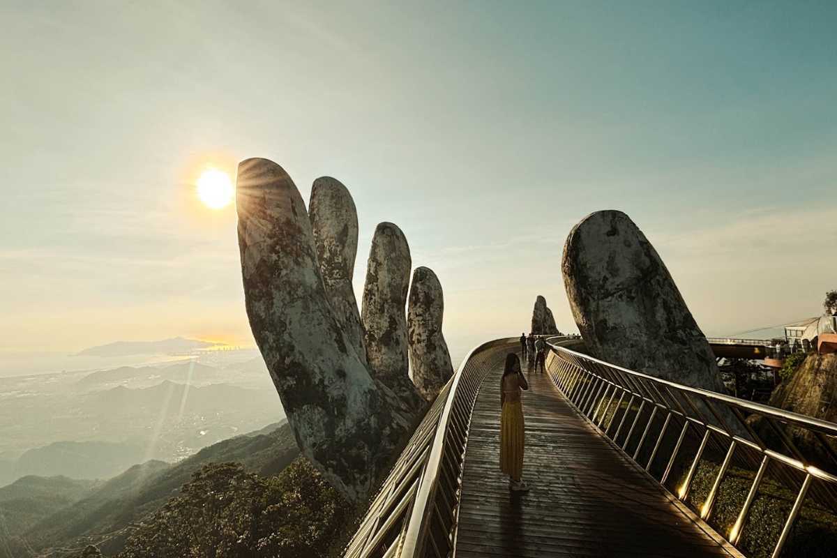 Golden Bridge Da Nang sunlit perspective with tourists Tourists walk Golden Bridge Da Nang with sunlit hands, curved path, and distant mountain background