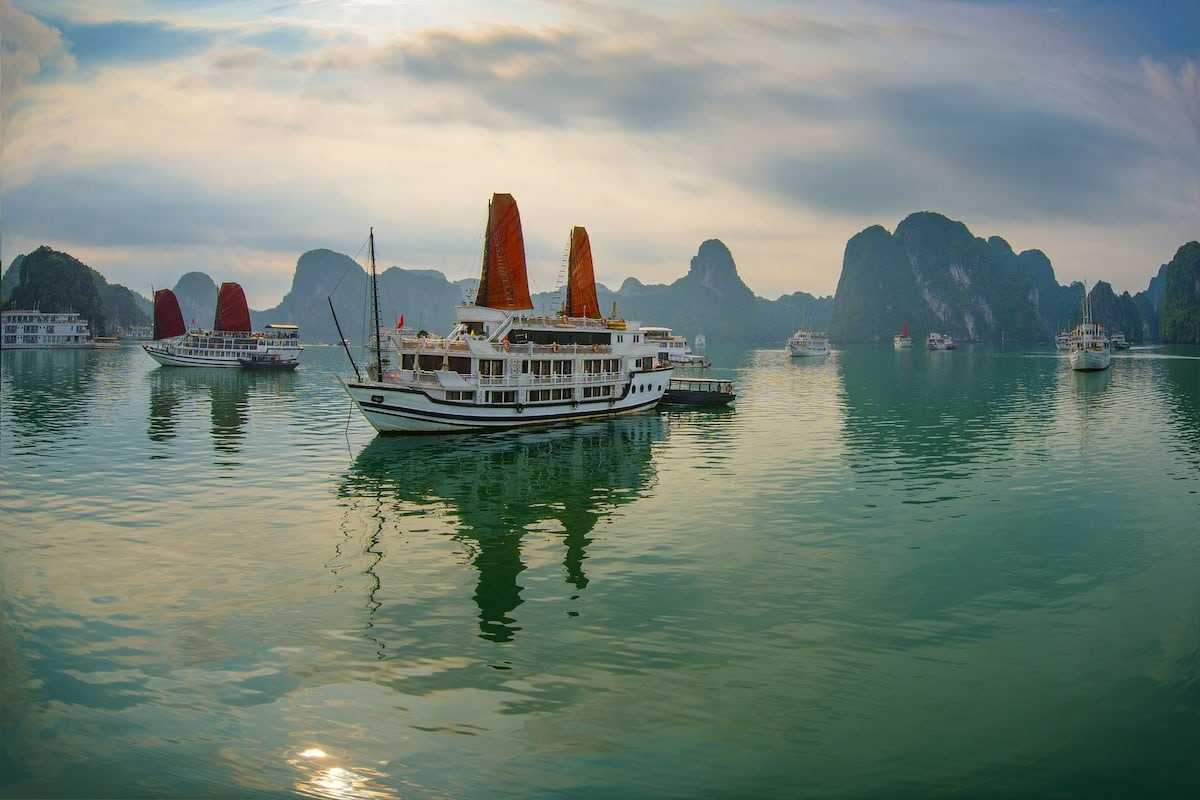 Ha Long Bay Cruise Boats with Limestone Islands Ha Long Bay cruise boats sailing on emerald waters surrounded by towering limestone karsts under a cloudy sky.