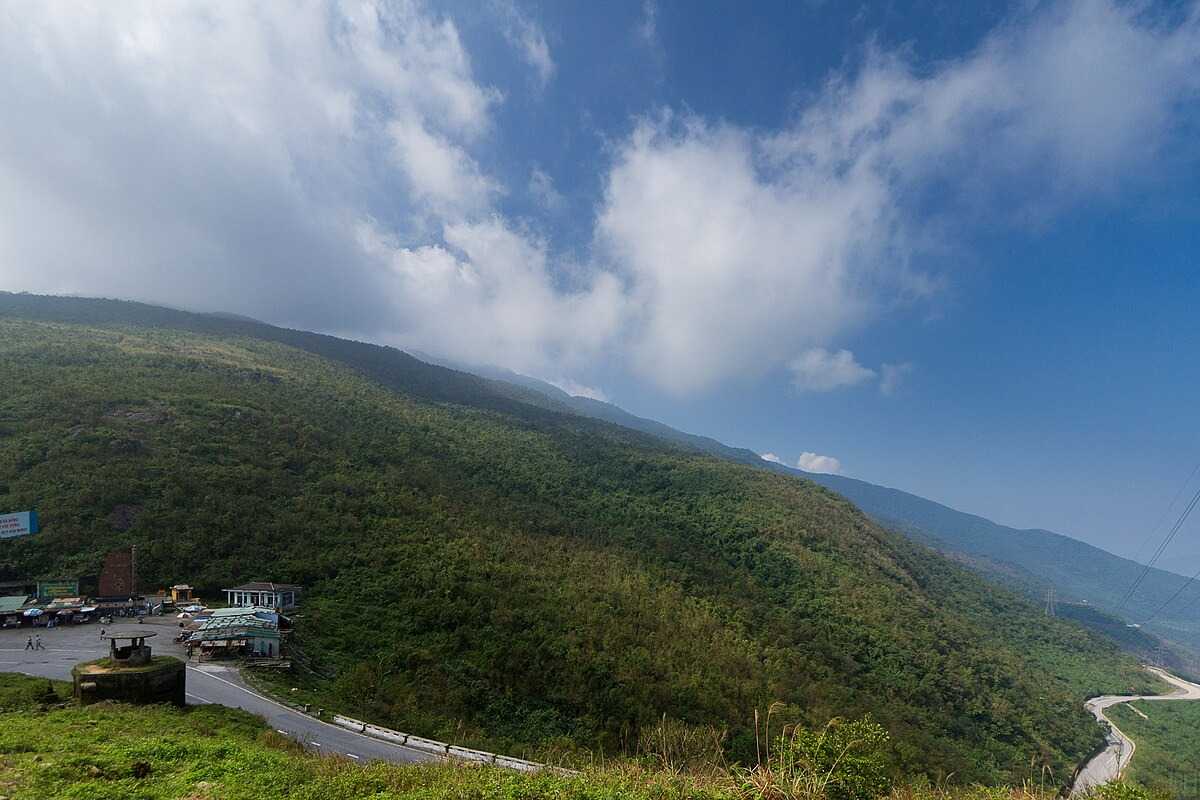 Hai Van Pass Da Nang panoramic view with roadside stop Hai Van Pass Da Nang offers a panoramic view of green mountains and a roadside rest area under a partly cloudy sky.