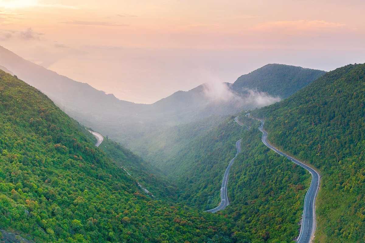 Hai Van Pass sunrise panorama misty mountain road Hai Van Pass sunrise panorama shows misty mountain roads and lush green valleys under soft morning light.