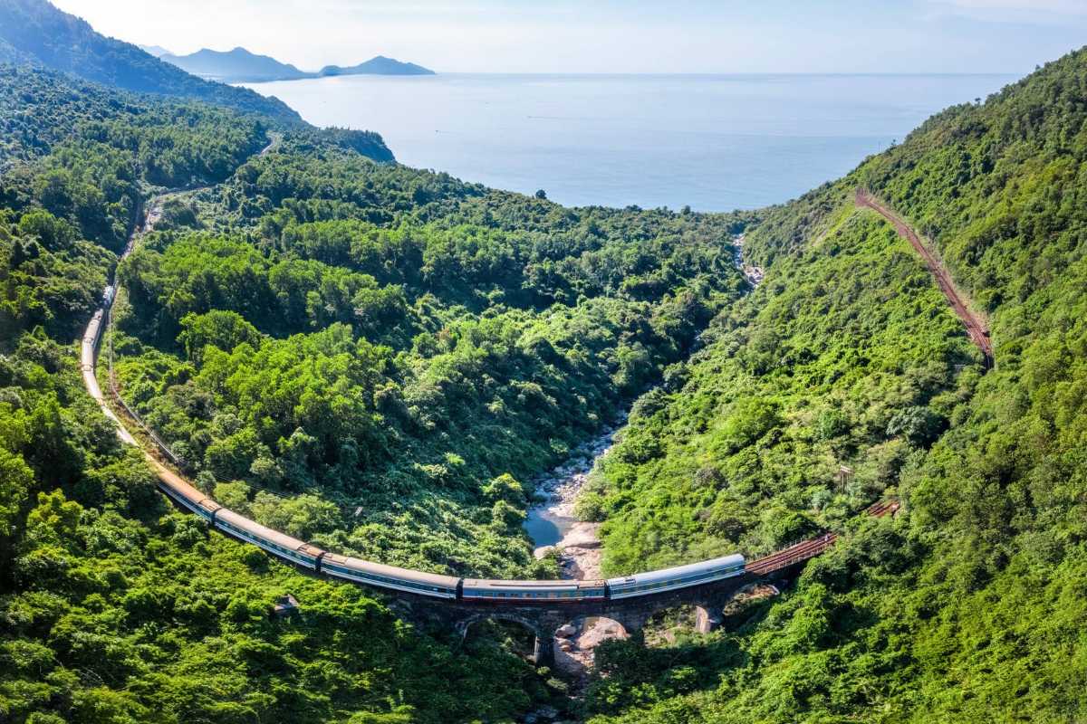 Hai Van Pass train bridge mountain valley journey Hai Van Pass showcases a train crossing a scenic bridge over a green valley, surrounded by hills and sea views.