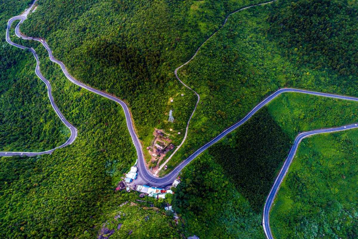 Hai Van Pass Vietnam aerial winding mountain road Hai Van Pass Vietnam features a dramatic aerial view of winding mountain roads surrounded by lush green forest.