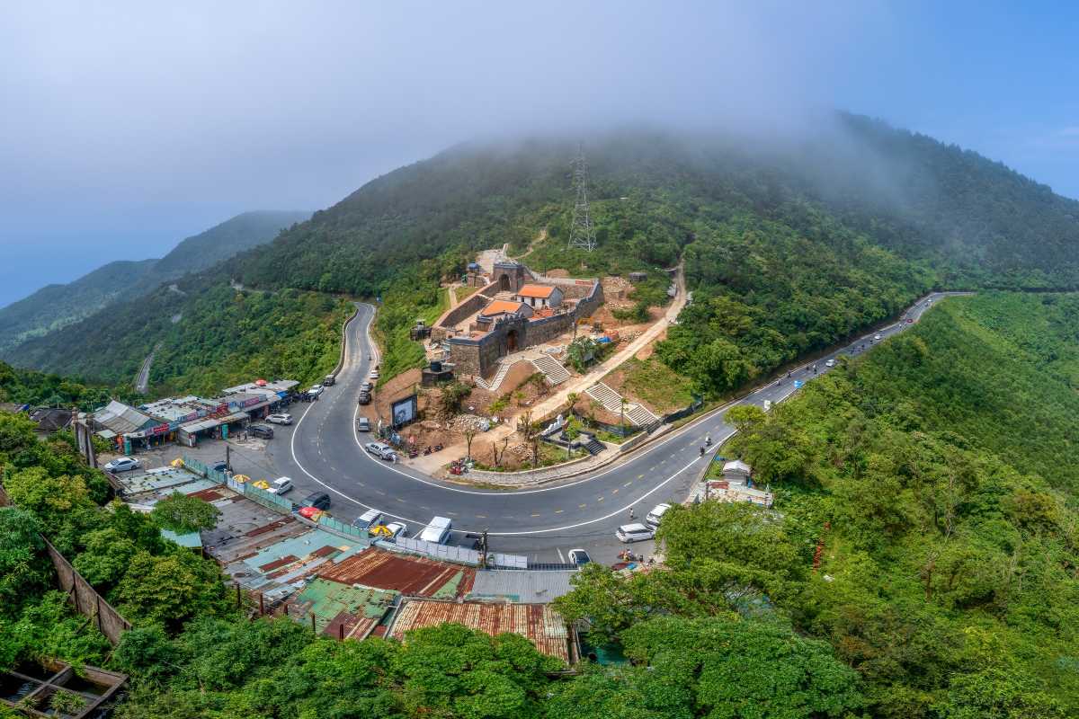 Hai Van Quan Gate mountain pass foggy summit view Hai Van Quan Gate on Hai Van Pass appears at the summit, surrounded by mist, green forests, and winding mountain roads.