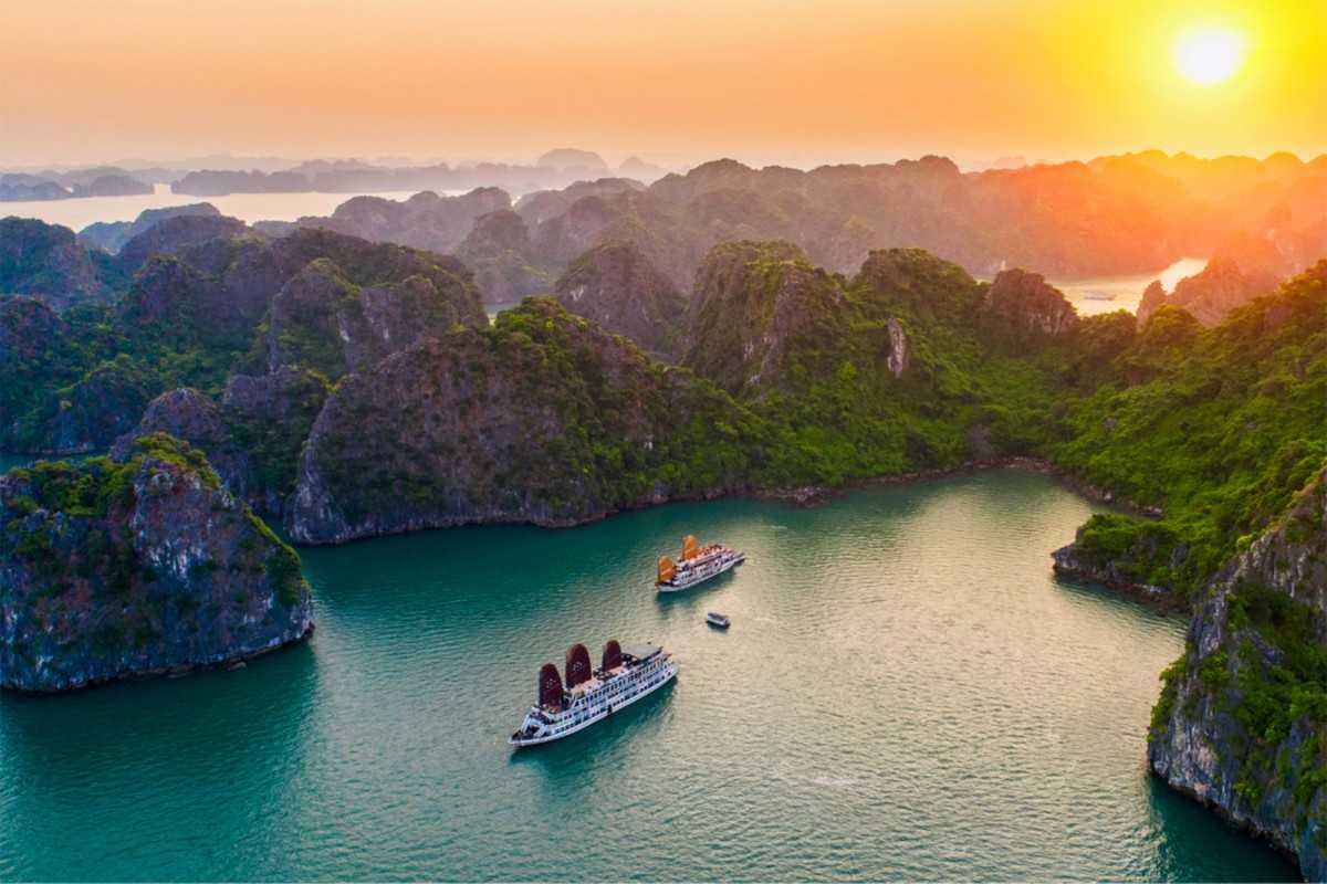 Close-up of Halong Bay cruise ship during sunset A large cruise ship with orange sails sails near limestone cliffs as the Halong Bay sunset paints the sky.