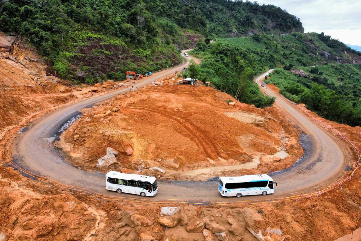 Under-construction curve on Heaven Pass Buses turning on red-dirt road segment under construction on Heaven Pass mountain pass.