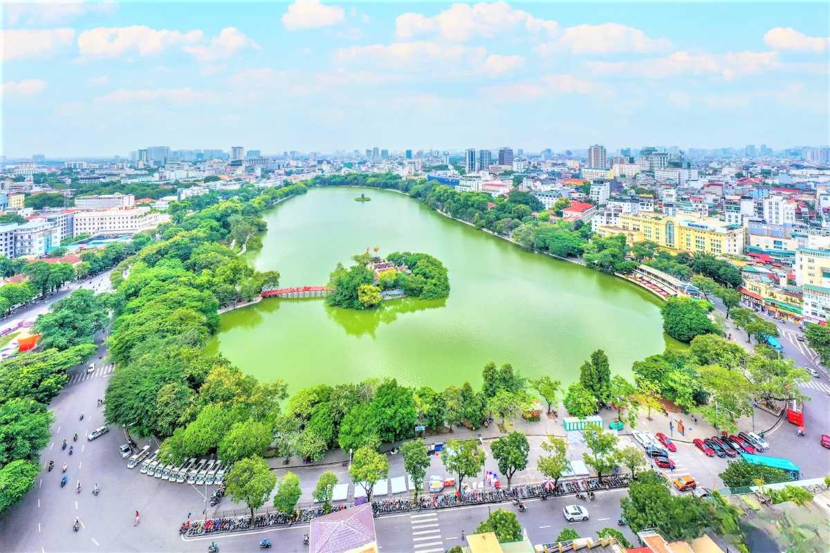 Woman Wearing Ao Dai on The Huc Bridge Hoan Kiem Lake Woman dressed in traditional white Ao Dai walking on red The Huc Bridge over Hoan Kiem Lake Hanoi with calm water below.