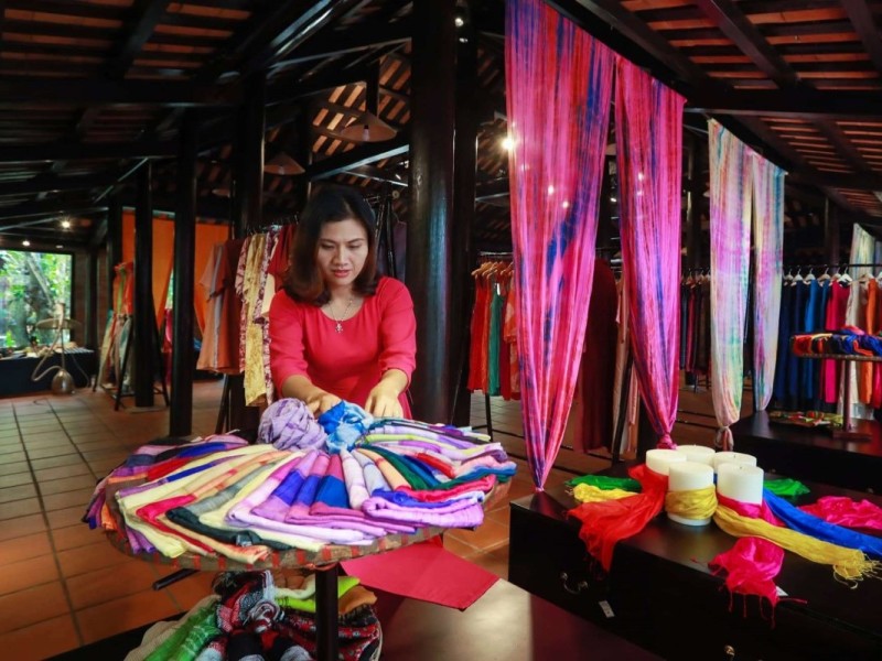 Artisan at Hoi An Silk Village arranging colorful silk scarves on display