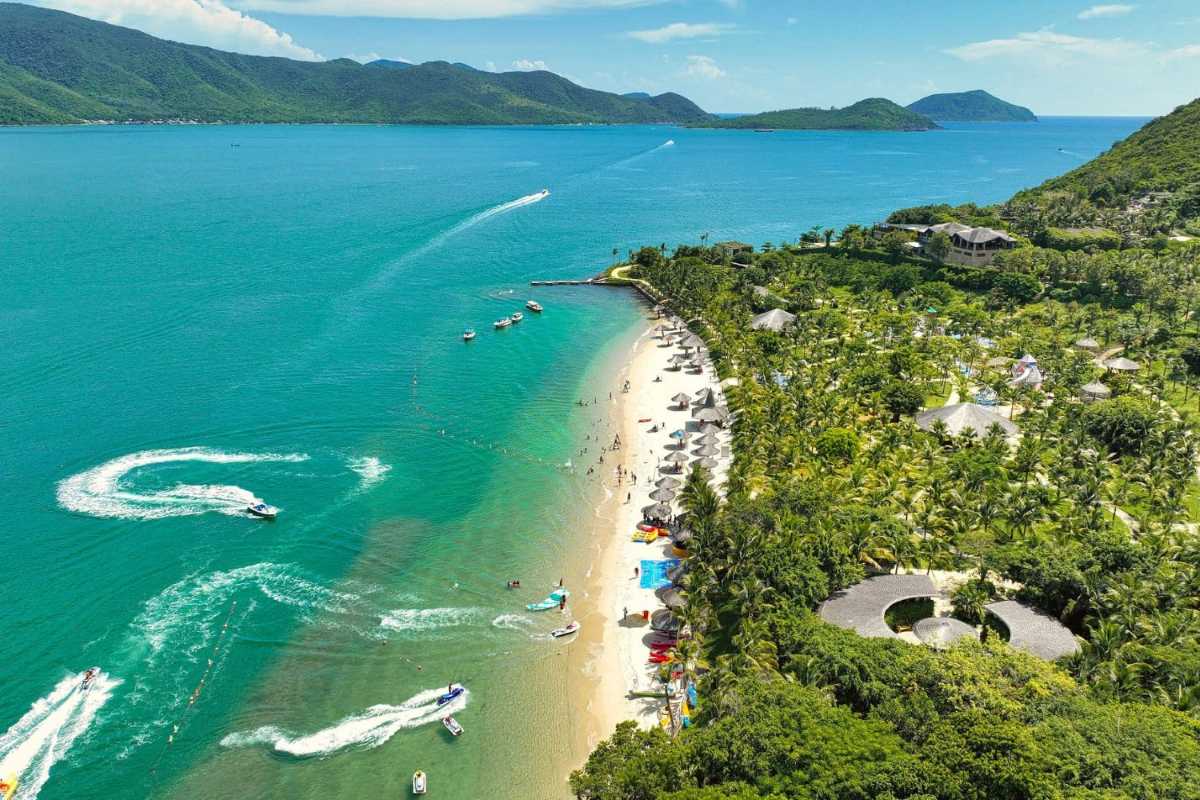 Vibrant beach activities on Hon Mun Island Visitors enjoying beach activities along the shoreline of Hon Mun Island’s resort with lush green hills behind.