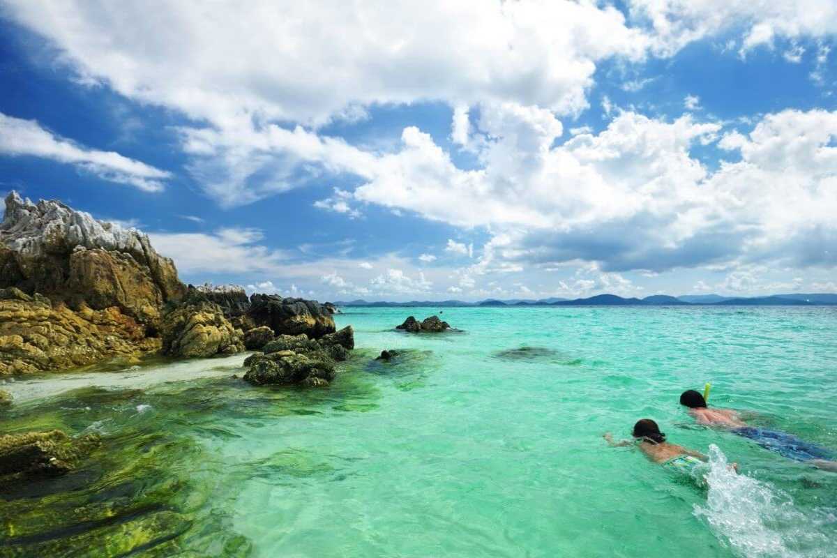 Snorkeling in crystal waters at Hon Mun Island Two snorkelers in clear turquoise water near rocky outcrops of Hon Mun Island under a partly cloudy sky.
