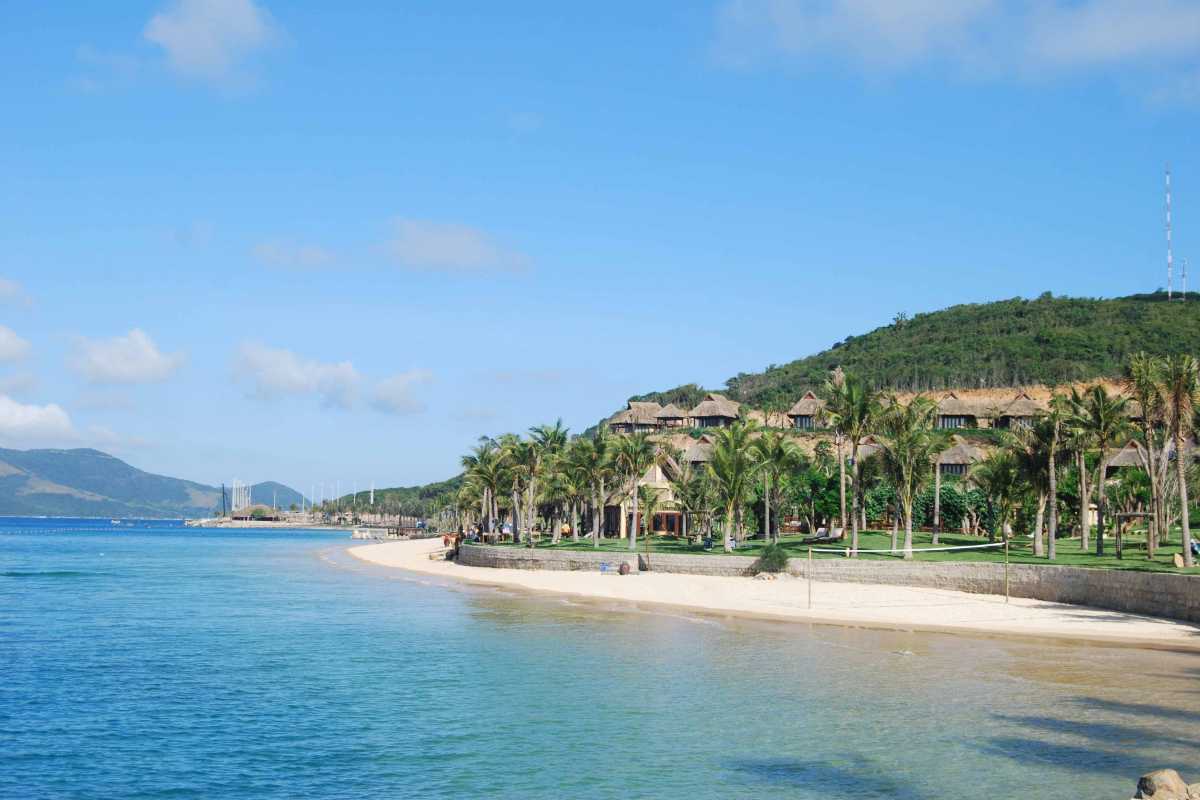 Resort villas on Hon Tam Island by the beach Palm trees and thatched-roof resort villas line the beachfront of Hon Tam Island under blue skies.