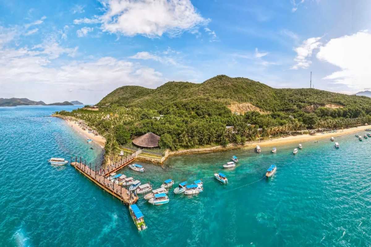 Hon Tam Island pier and boats aerial view Dozens of boats docked near Hon Tam Island's wooden pier surrounded by lush greenery and beaches.