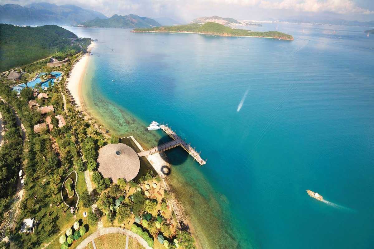 Hon Tam Island dock and ocean view Aerial photo of Hon Tam Island pier stretching into calm blue waters with coastal mountains nearby.