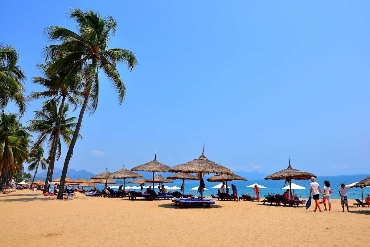 Palm-lined sandy beach on Hon Tam Island Visitors relax under thatched umbrellas on Hon Tam Island's golden beach lined with palm trees.