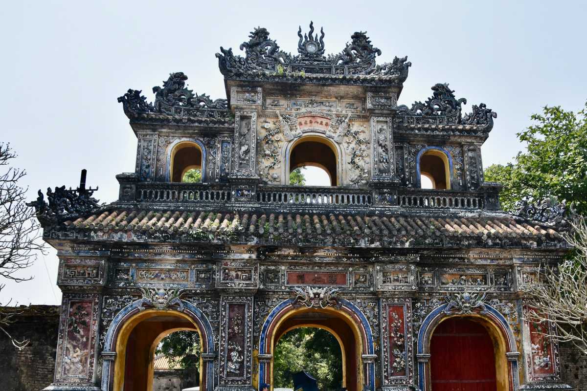 Ornate ancient gate at Hue Imperial City Ornate three-arched stone gate adorned with intricate carvings at Hue Imperial City, set against a clear sky and lush trees.