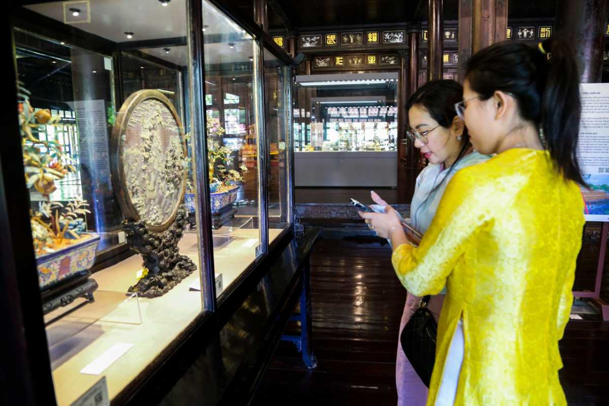 Visitors viewing exhibits at Hue Museum of Royal Antiquities Two visitors in ao dai viewing Nguyen Dynasty exhibits at Hue Museum of Royal Antiquities, traditional Vietnamese museum scene
