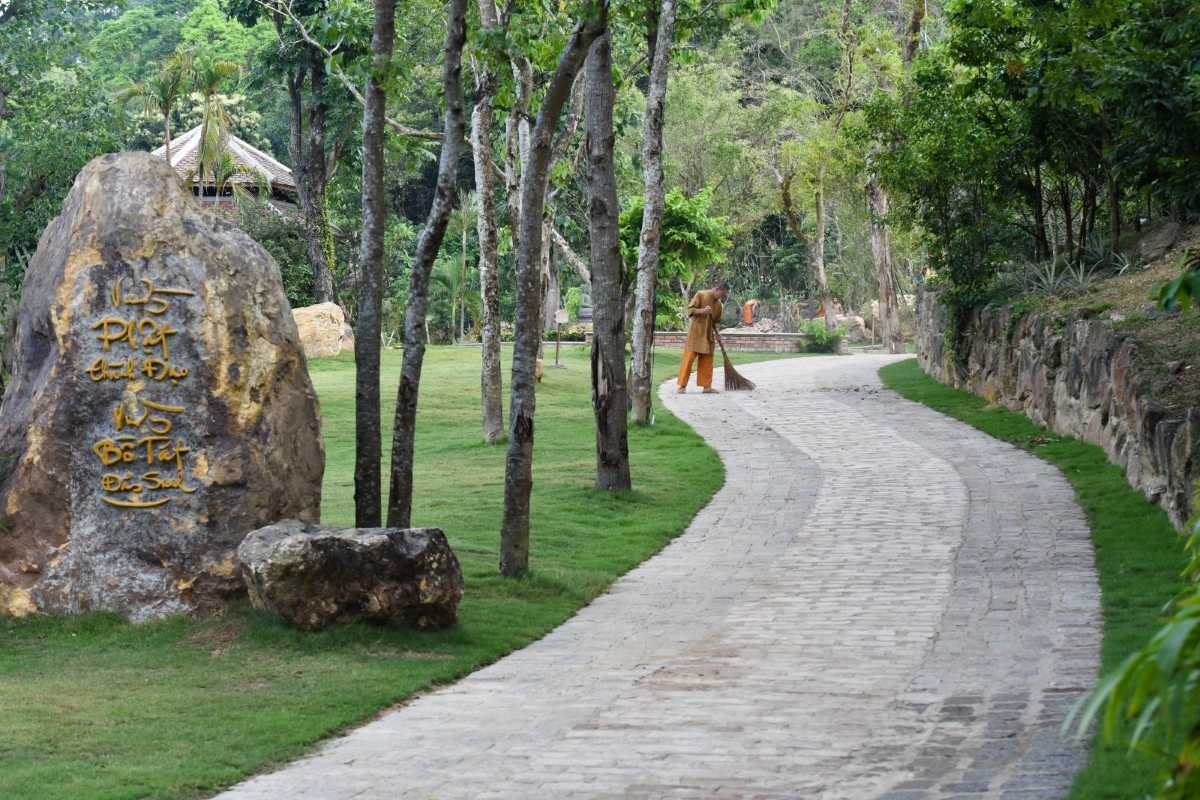 Huyen Khong Son Thuong Pagoda Hue tranquil path with monk and engraved rock Huyen Khong Son Thuong Pagoda Hue tranquil stone path lined with trees, Buddhist monk sweeping, large engraved rock in foreground