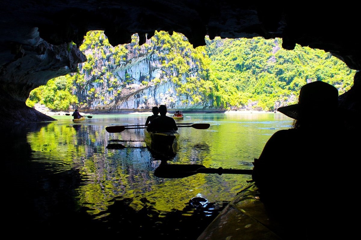 Kayakers paddling through the serene waters of Dark and Light Caves in Ha Long Bay, surrounded by limestone cliffs.