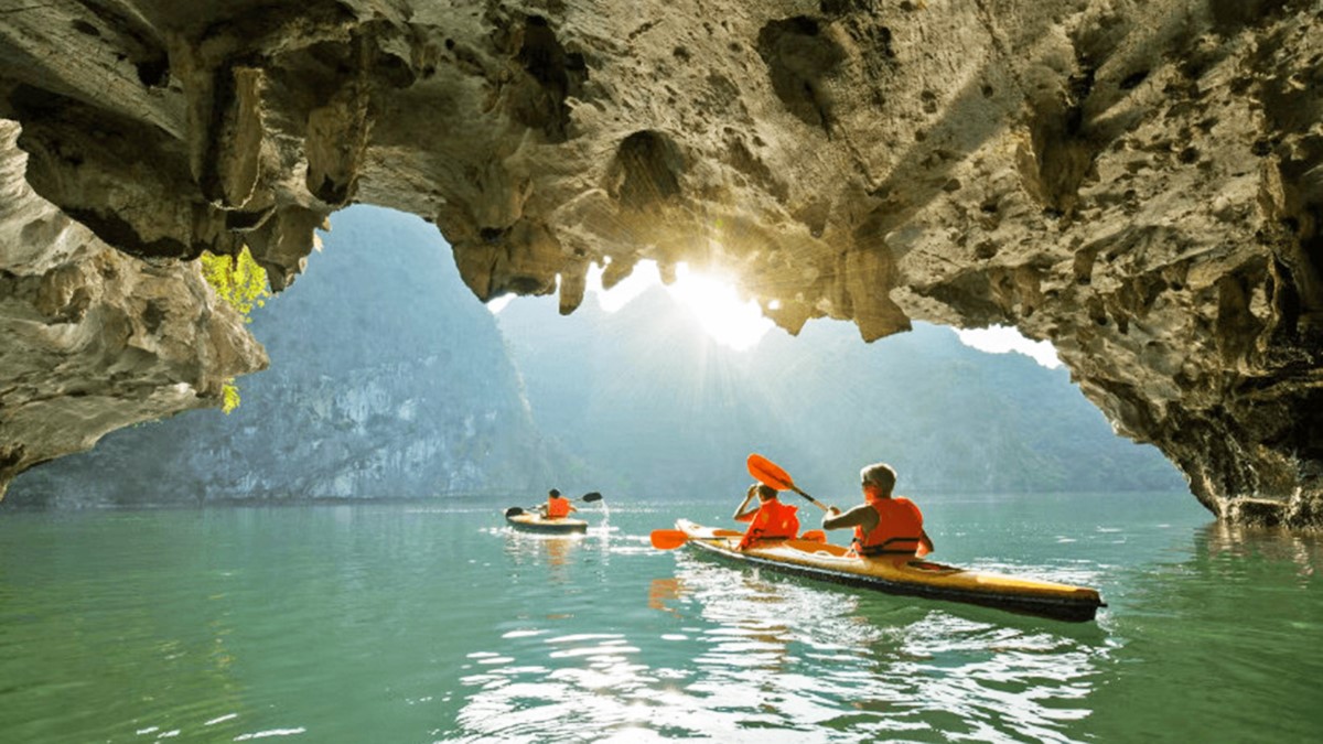 A group of tourists kayaking through the tranquil waters of Luon Cave in Halong Bay, surrounded by towering limestone cliffs.