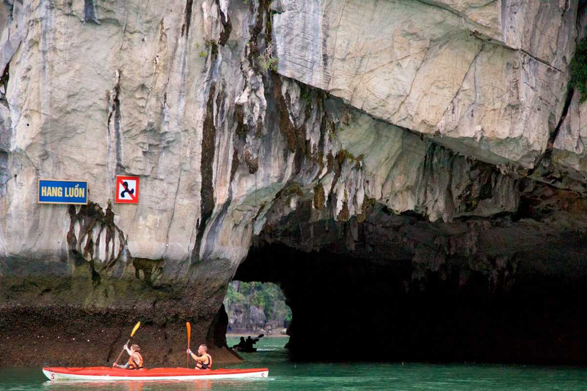 Kayaking Luon Cave Halong Bay limestone archway entry Kayakers paddling under a rugged limestone archway at Luon Cave in Halong Bay
