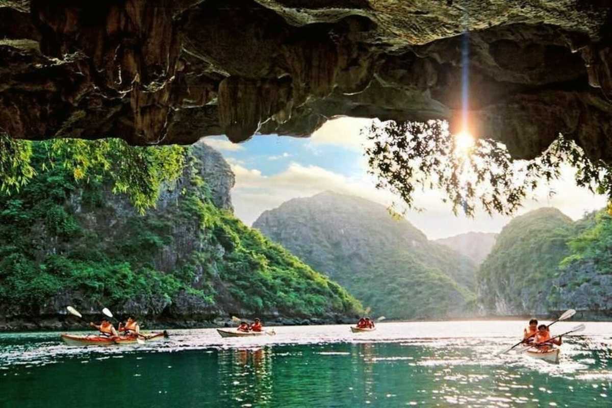 Kayaking Luon Cave Halong Bay serene water approach Kayakers paddling calmly on emerald water near Luon Cave entrance framed by limestone cliffs