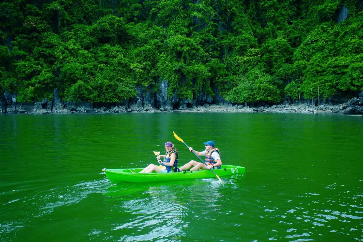 Kayaking Luon Cave Halong Bay shadowed cave entry Kayaker entering shadowed cave opening surrounded by limestone in Luon Cave Halong Bay