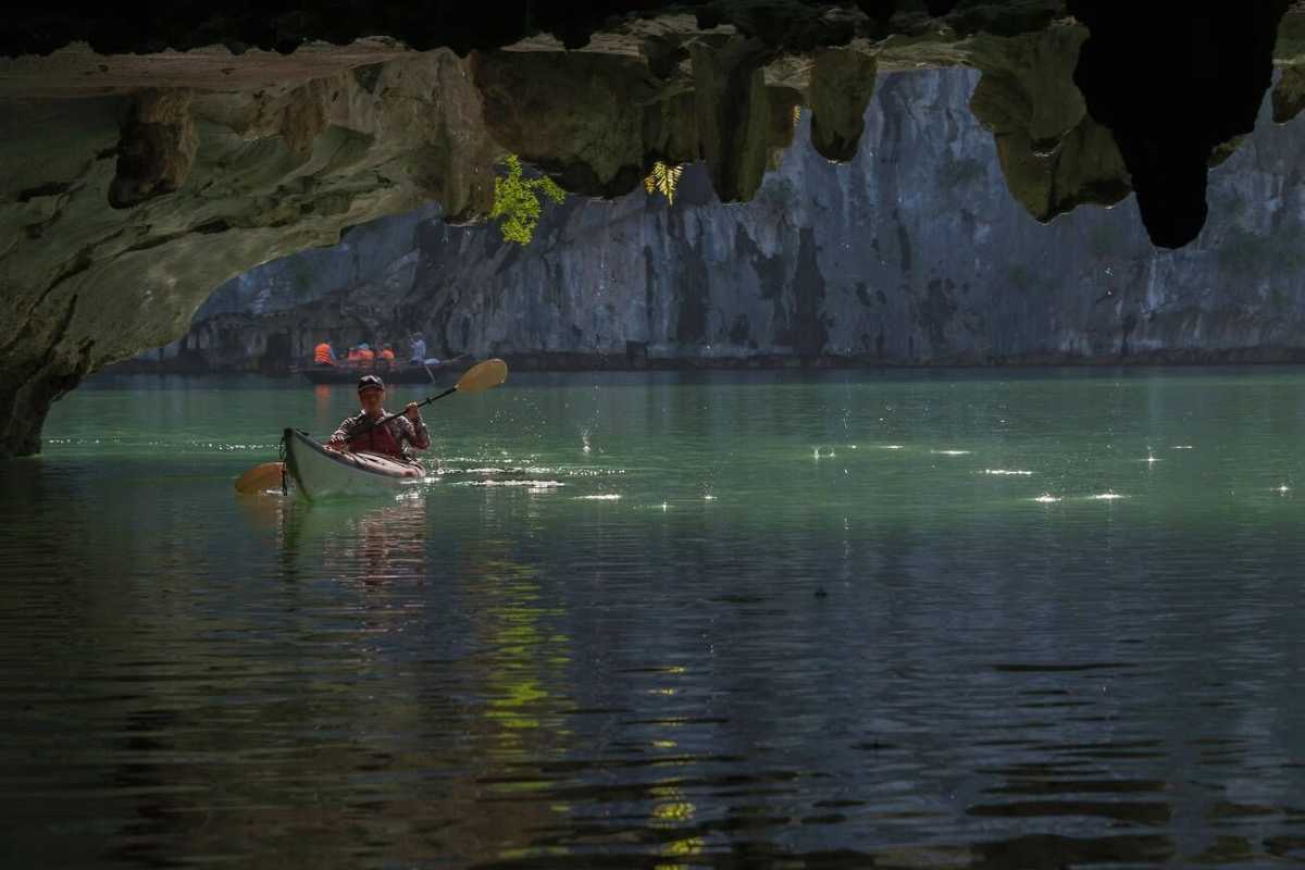 Kayaking Luon Cave Halong Bay solo kayak inside cave Solo kayaker paddling inside Luon Cave with sunlight filtering through limestone formations