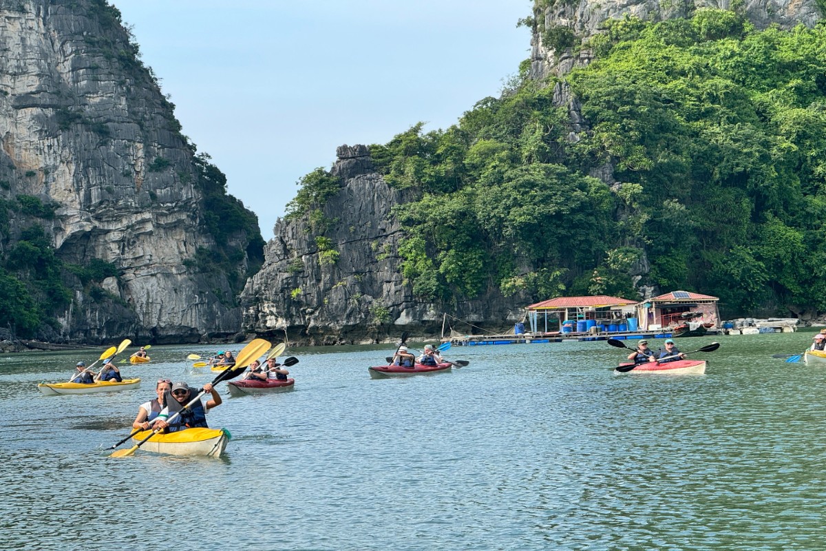 A group kayaking through the tranquil waters of Cua Van Fishing Village, surrounded by limestone karsts