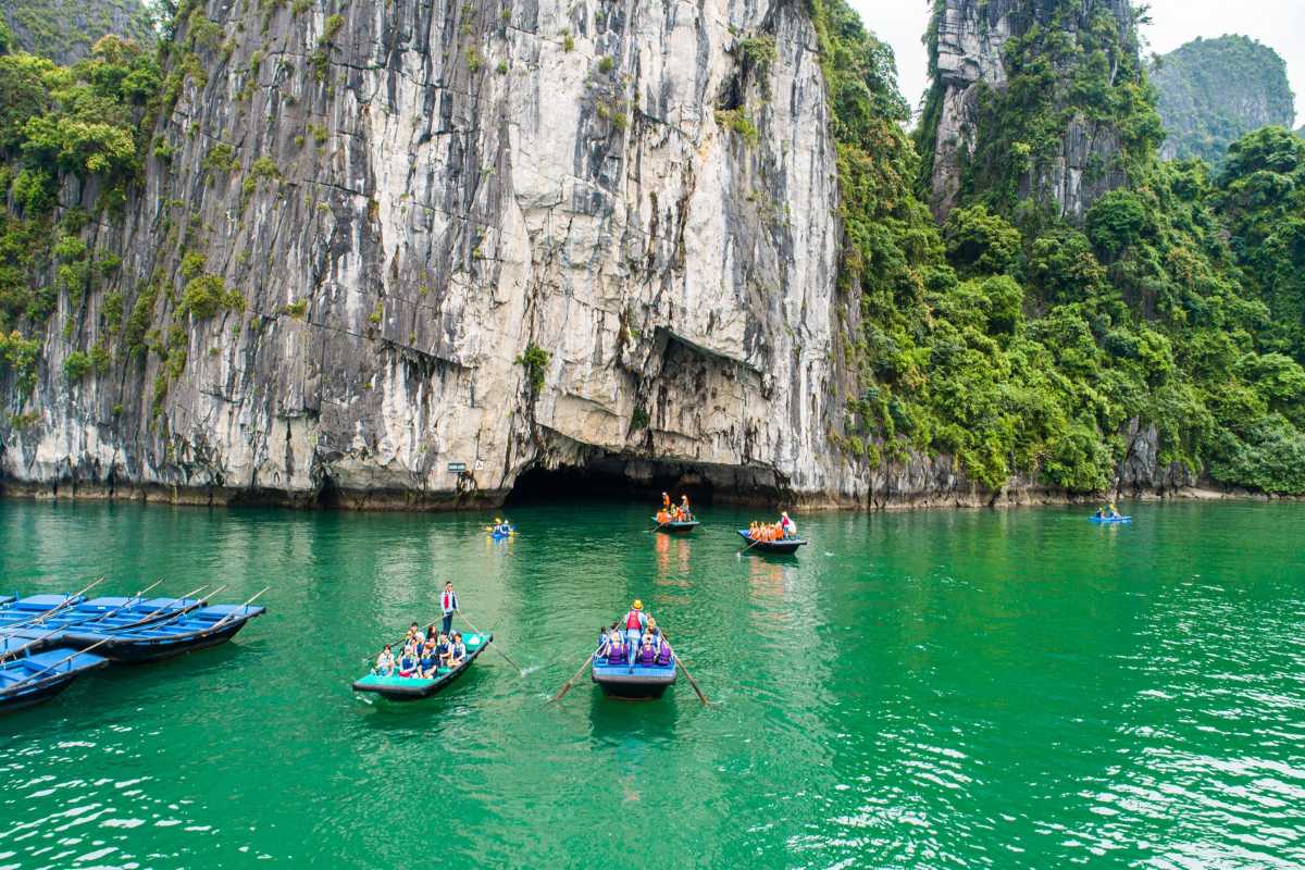 Lan Ha Bay Vietnam boat cave entrance kayaking scene Tourists row boats and kayak toward a cave entrance surrounded by steep limestone cliffs in Lan Ha Bay Vietnam