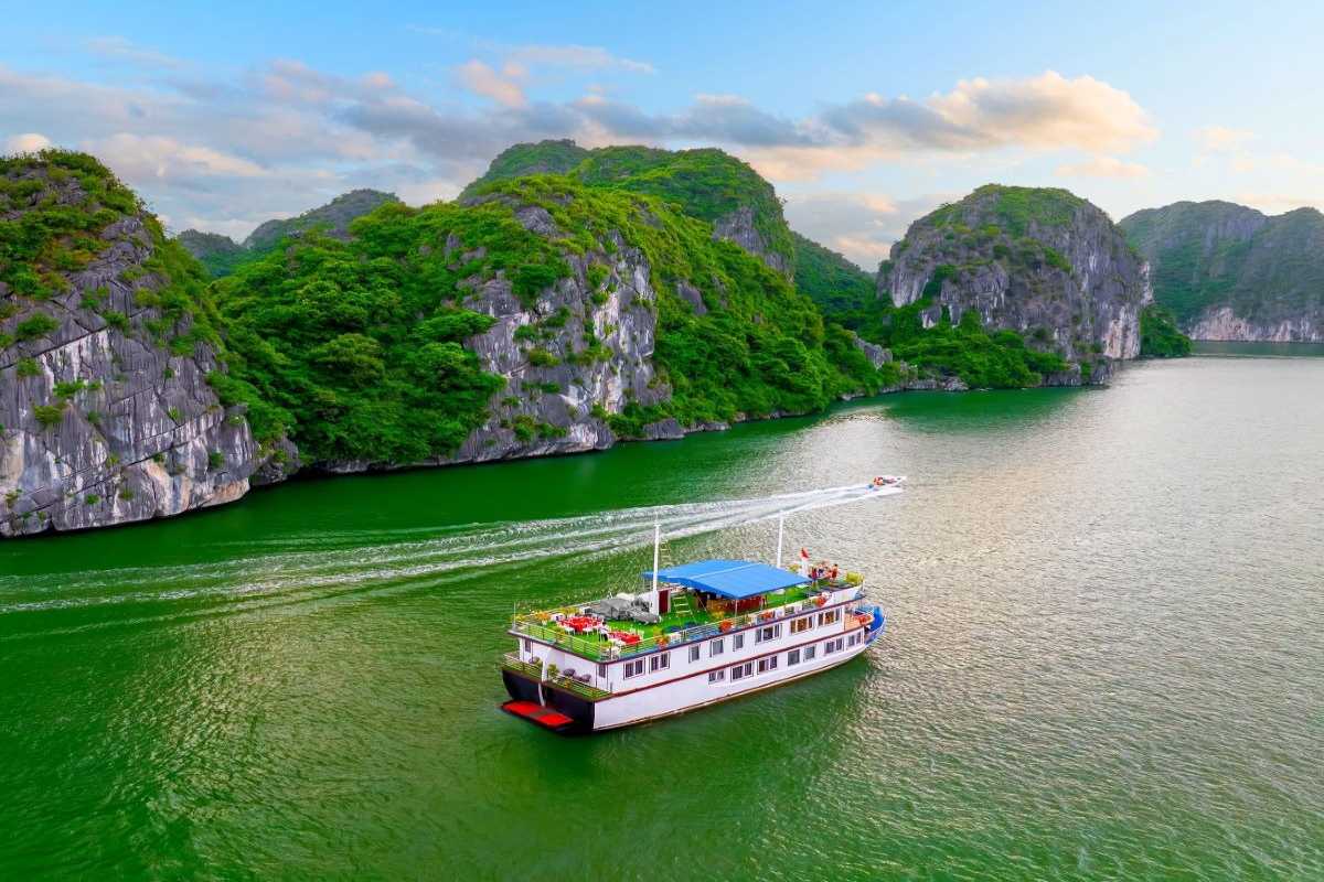 Lan Ha Bay Vietnam classic wooden boat cruise A traditional-style wooden cruise boat sails through lush green karst islands in Lan Ha Bay Vietnam