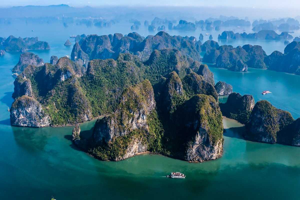 Lan Ha Bay Vietnam cruise ship sailing near cliffs A white cruise ship sails peacefully near steep limestone cliffs in Lan Ha Bay’s calm waters.