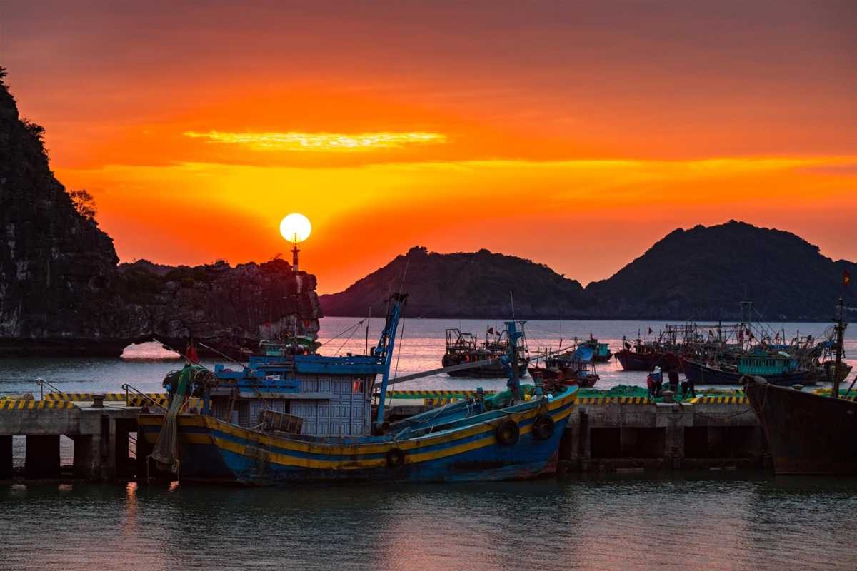 Lan Ha Bay Vietnam fishing harbor at colorful sunset Traditional fishing boats docked at a harbor with a vivid orange sunset over Lan Ha Bay Vietnam