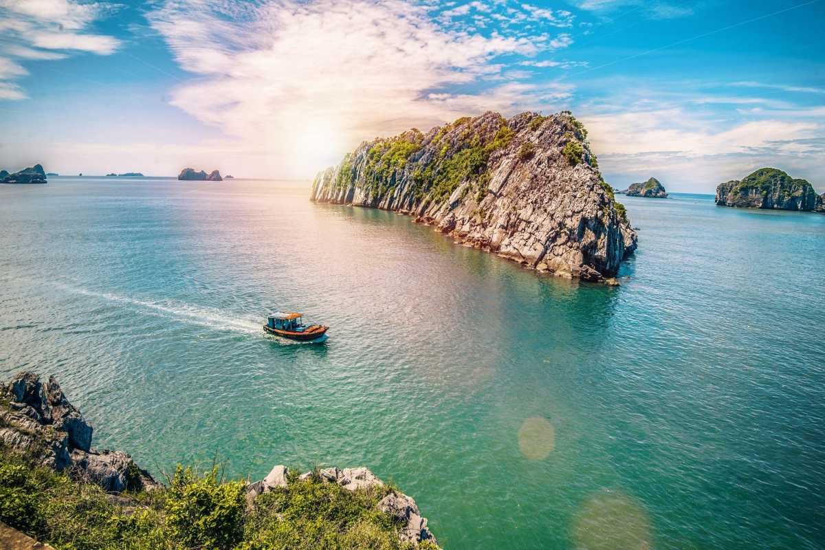 Lan Ha Bay Vietnam traditional junk boat near rocky islets A traditional Vietnamese junk boat sails close to jagged islets in Lan Ha Bay’s pristine water.