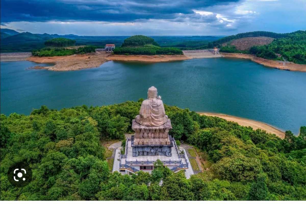 Lang Co Beach Hue Buddha statue overlooking tranquil reservoir Lang Co Beach Hue displays a giant Buddha statue surrounded by forest, facing a serene lake, highlighting spiritual and natural harmony.