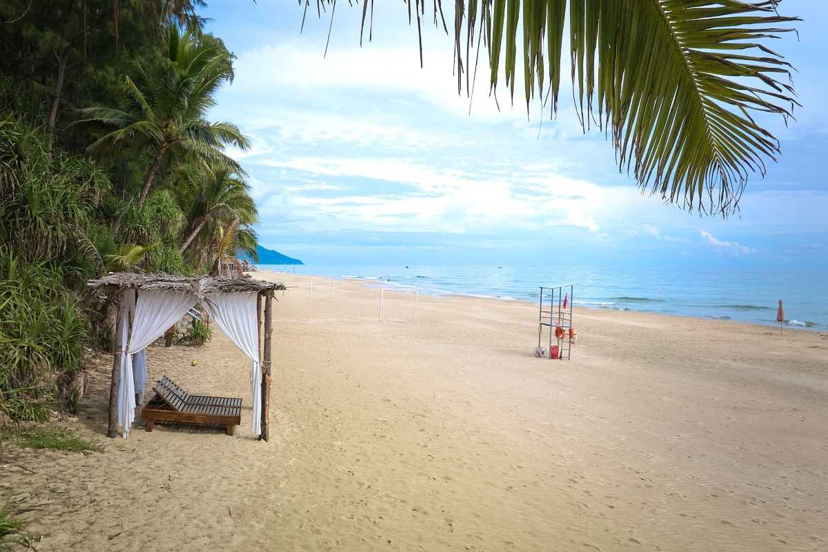 Lang Co Beach Hue shaded cabana and pristine sandy shoreline Lang Co Beach Hue features a rustic wooden cabana under palm trees beside a long, pristine sandy beach, perfect for a peaceful getaway.