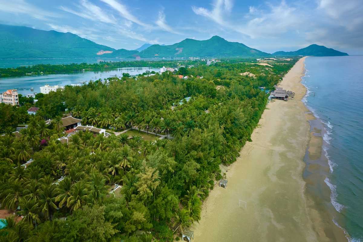 Lang Co Beach Hue panoramic view of coastline and lush mountains Lang Co Beach Hue offers a wide coastal vista, with dense green trees, sandy shoreline, and dramatic mountain backdrop under blue skies.
