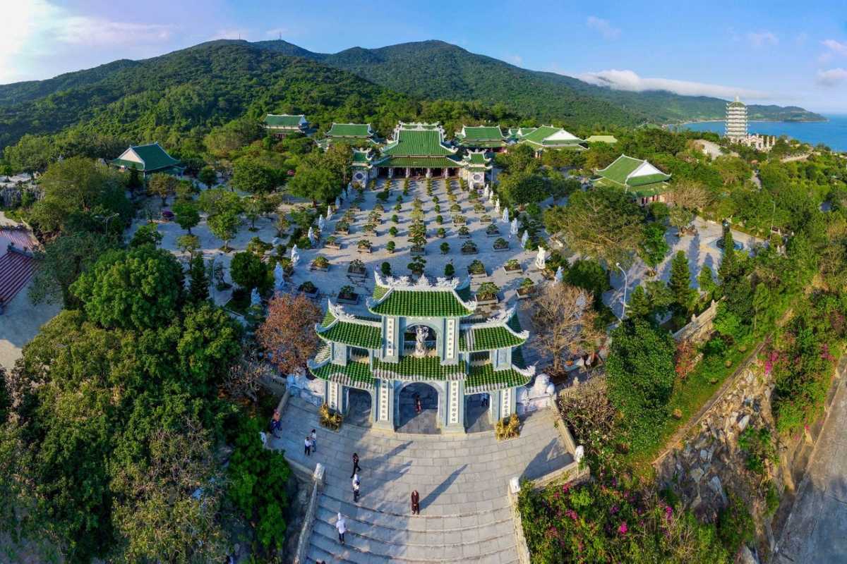 Linh Ung Pagoda Da Nang aerial temple complex and mountain view Linh Ung Pagoda Da Nang aerial view shows temple courtyards, green-tiled roofs, and Son Tra mountain in the background.