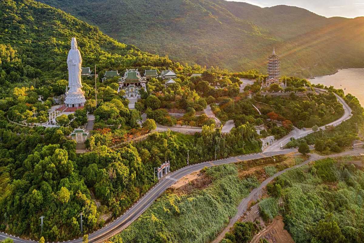 Linh Ung Pagoda Da Nang aerial view with Lady Buddha and coastline Linh Ung Pagoda Da Nang aerial photo shows Lady Buddha statue, temple buildings, winding roads, and coastline during golden sunset.