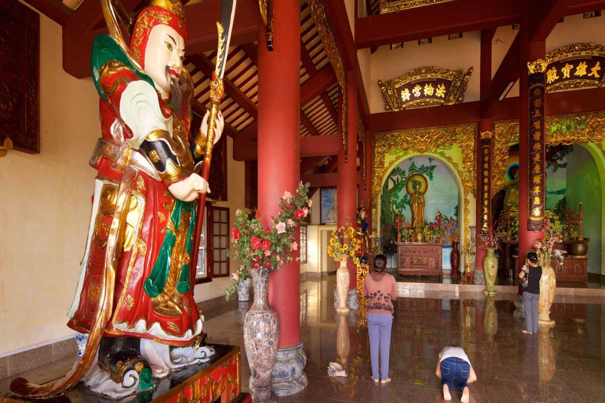 Linh Ung Pagoda Da Nang grand hall statue and worshippers scene Linh Ung Pagoda Da Nang features an ornate guardian statue and worshippers praying inside the grand hall with vibrant decorations.