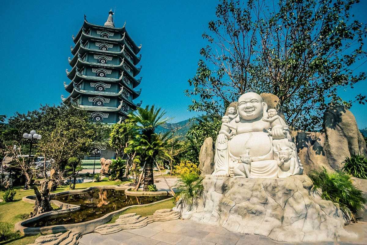 Linh Ung Pagoda Da Nang smiling Buddha statue and pagoda tower Linh Ung Pagoda Da Nang’s marble smiling Buddha statue sits near a multi-story pagoda tower surrounded by a peaceful garden.