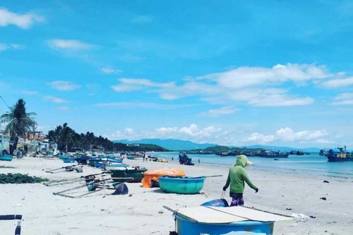 People walking and working along Ninh Thuy Fishing Village sandy beach Locals walking and preparing fishing gear on the sandy beach of Ninh Thuy Fishing Village under clear blue skies