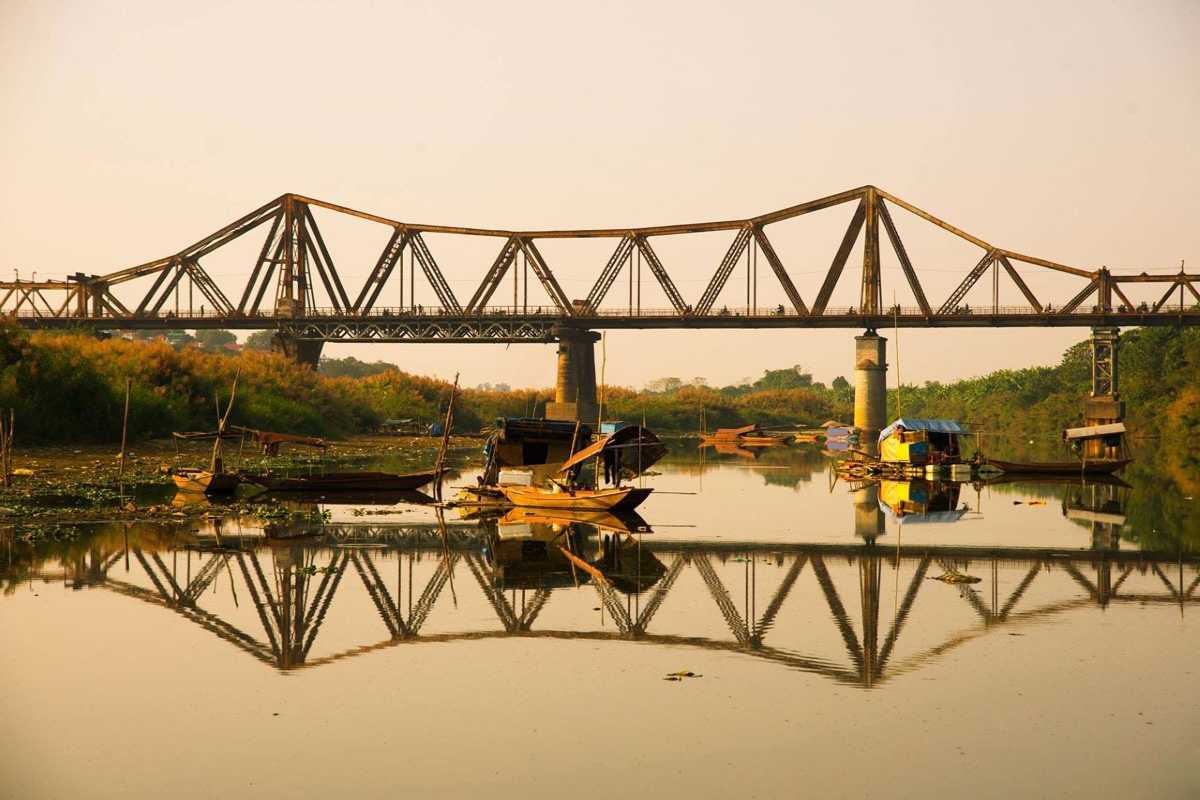 Long Bien Bridge Hanoi Scenic River View Scenic view of Long Bien Bridge over calm river with traditional boats reflecting in the water