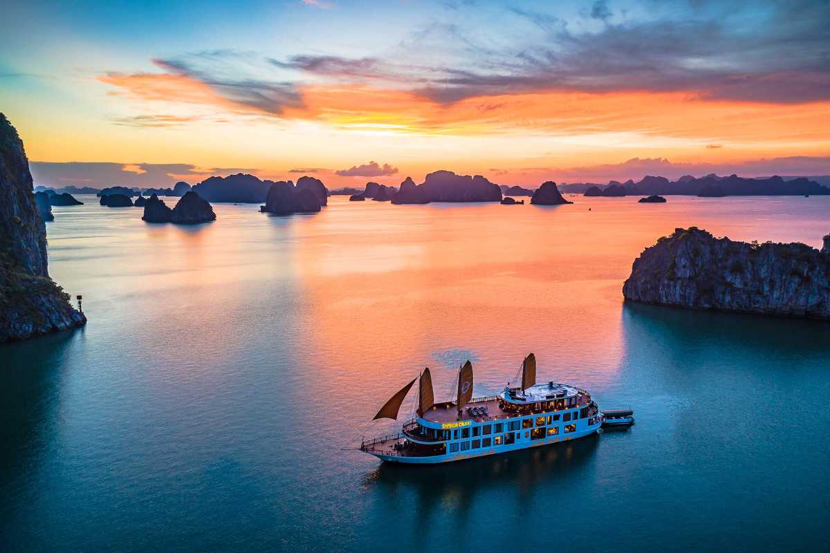 Luxury Halong Bay cruise under golden sky A luxury cruise with lit decks sails through Halong Bay as golden light reflects on the water and cliffs.